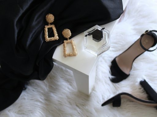 pair of gold-colored earrings on table and black ankle-strap pumps on area rug