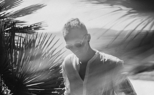 A man in a white shirt is walking by a palm tree