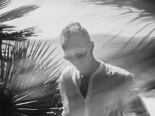 A man in a white shirt is walking by a palm tree