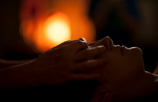 Hands massaging a person's face in a dimly lit room with warm bokeh