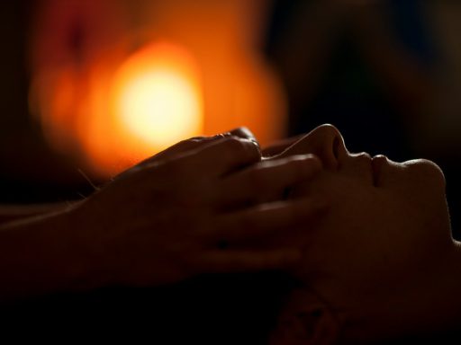 Hands massaging a person's face in a dimly lit room with warm bokeh