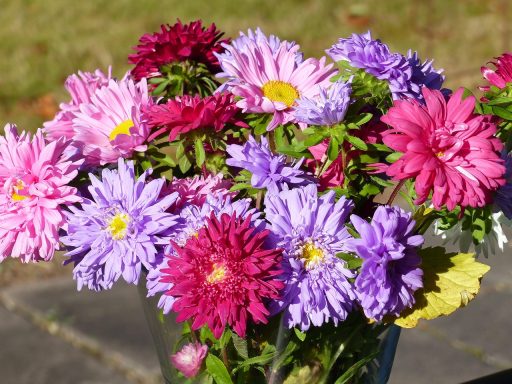 Vaas met herfstsnijbloemen in warme tinten oranje, bordeaux en geel op een houten tafel